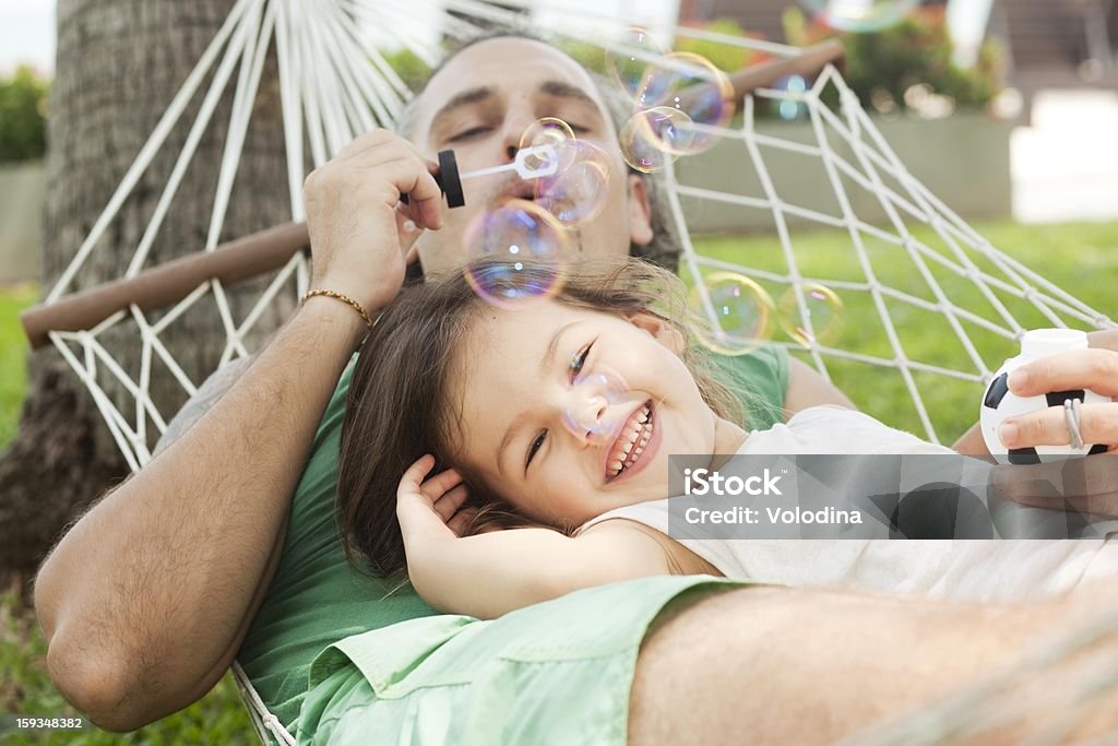 Father blowing bubbles with daughter in a hammock